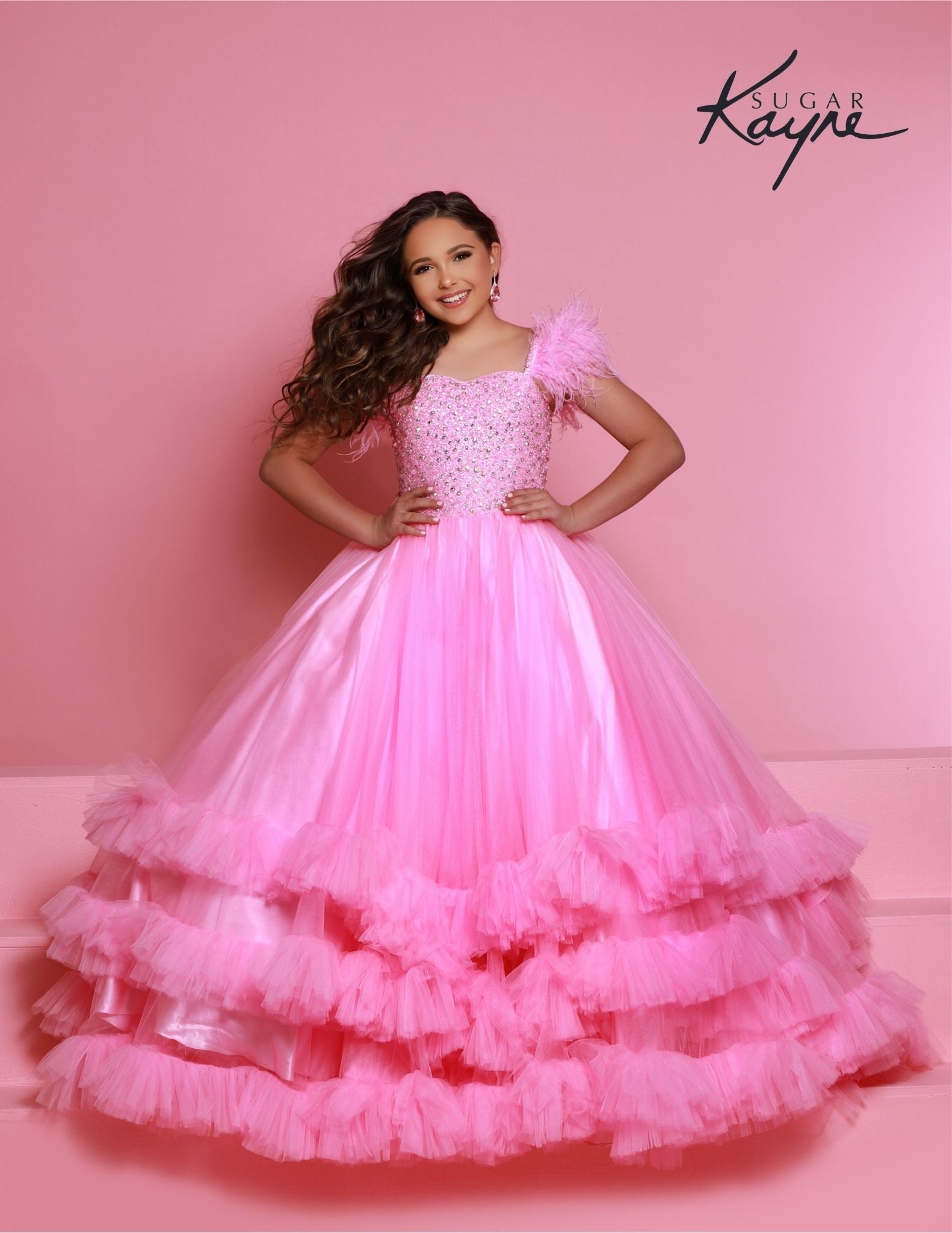 Sugar Kayne C327 features a fashionable bubblegum pageant dress for girls and preteens, complete with feather straps, a tiered ruffle bottom, and a crystal stone bodice.